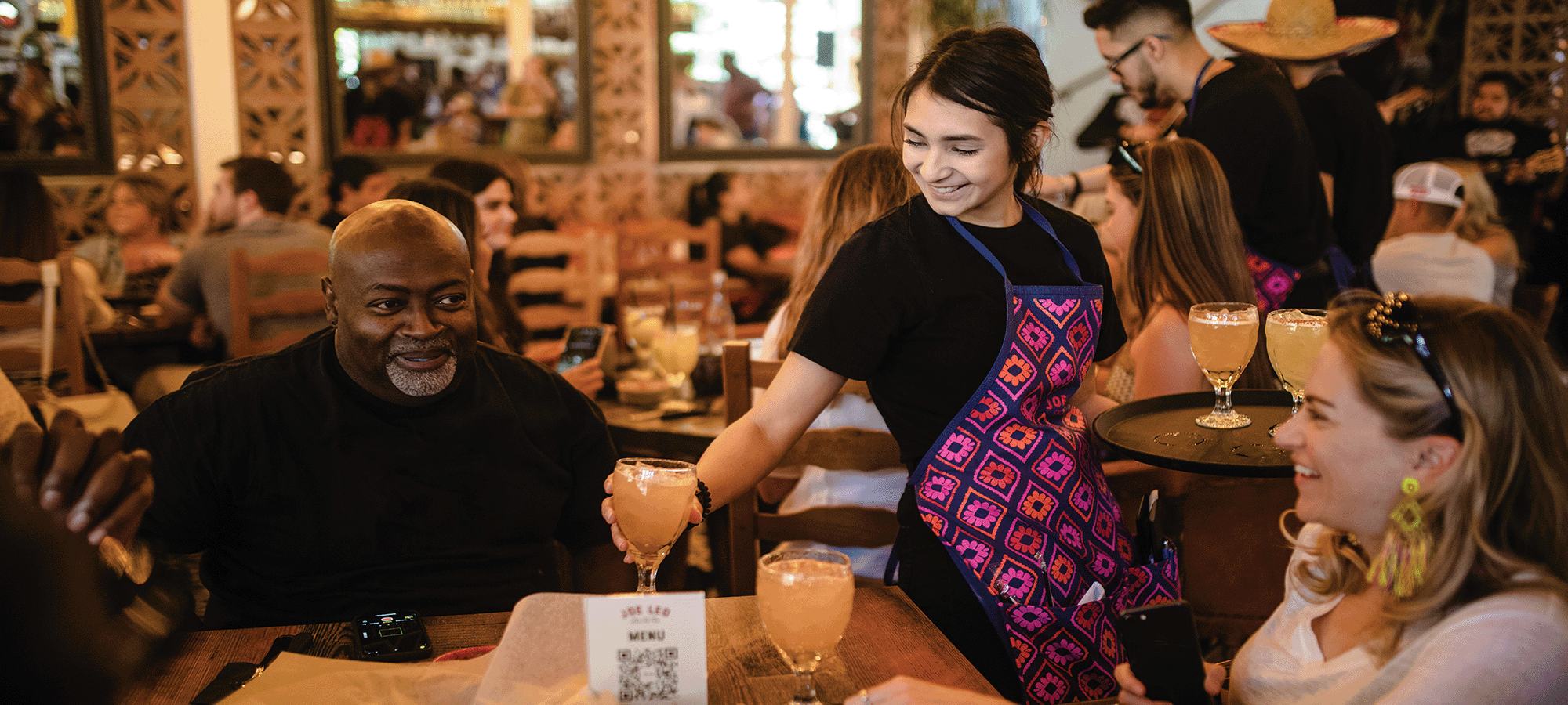 A Joe Leo waitress happily serves a smiling couple The People's Margarita.