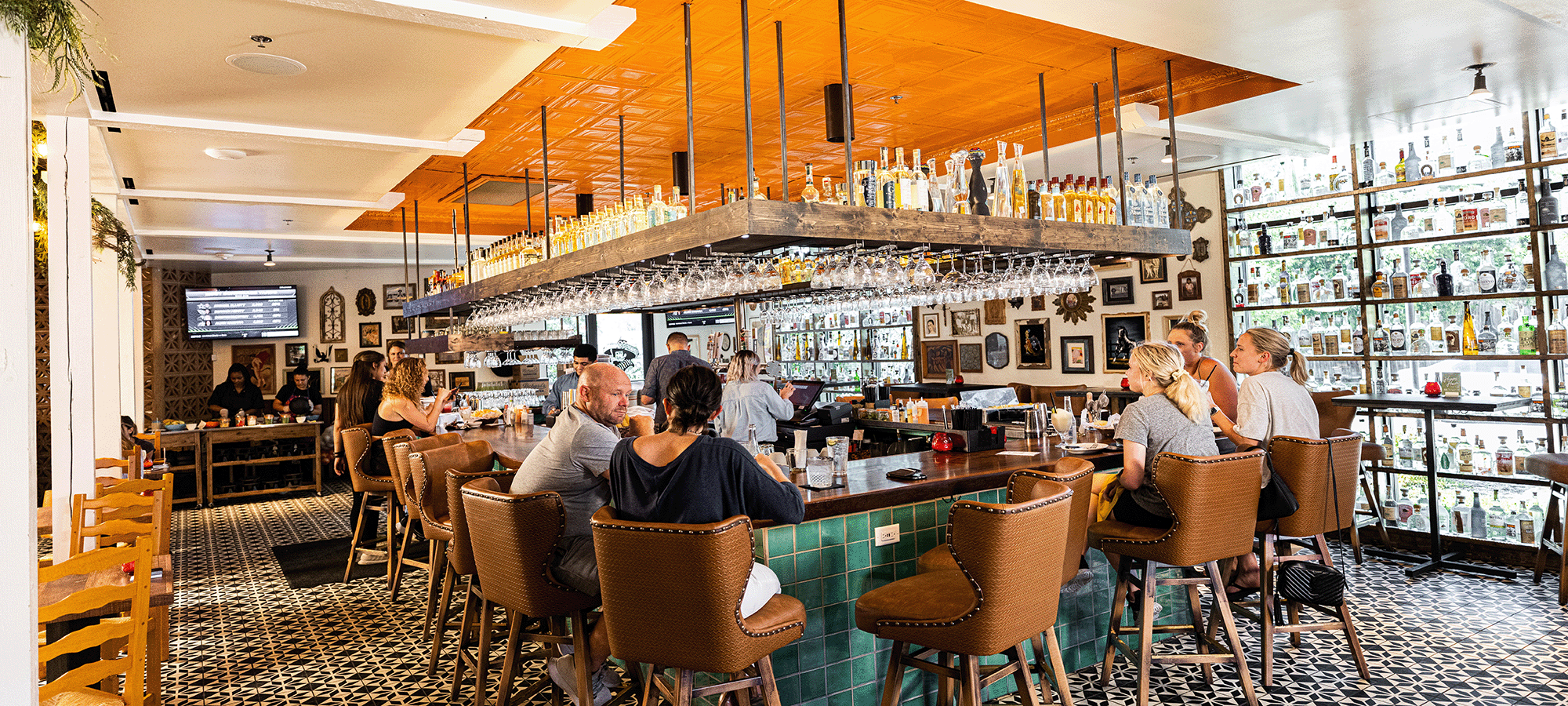 A group of people sit at the bar enjoying cocktails.