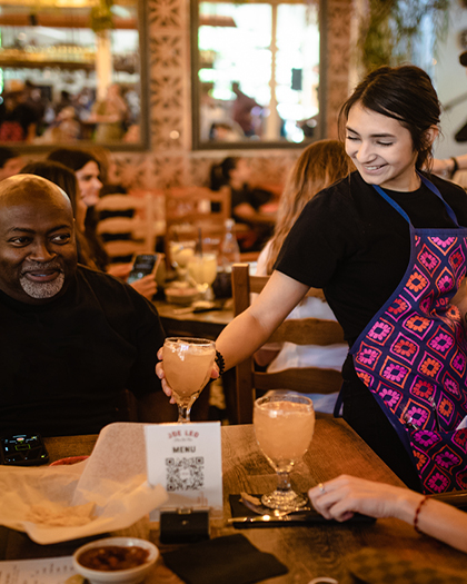 A Joe Leo waitress happily serves a smiling customer The People's Margarita.